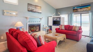 Una sala de estar con sofás rojos, una chimenea, un televisor y un balcón con cortinas.