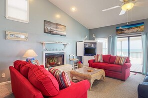 A living room with red sofas, a fireplace, a television, and a balcony with curtains. - Sunny oceanfront home with beach access, balcony, washer/dryer, & WiFi (Gulf Shores)