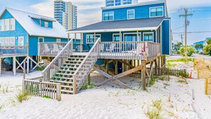Una propiedad frente a la playa con una terraza de madera, una escalera que conduce a un segundo nivel y vistas al océano.