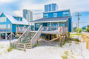 A beachfront property with a wooden deck, a staircase leading to a second level, and a view of the ocean. - Sunny oceanfront home with beach access, balcony, washer/dryer, & WiFi (Gulf Shores)
