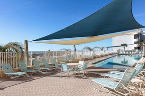 Ein Poolbereich mit Liegestühlen und einem Tisch, ein Schwimmbecken und ein Gebäude im Hintergrund.