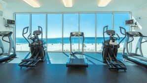 A gym with treadmills and elliptical machines, large windows with a beach view. - Gulf front beach condo with multiple community pools & sauna (Gulf Shores)