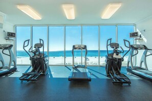 Ein Fitnessstudio mit Laufbändern und Crosstrainern, große Fenster mit Blick auf den Strand.