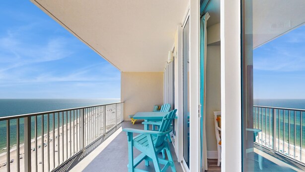 A balcony with a view of the beach and ocean, a table with chairs, and a glass door leading to another room. - Gulf front beach condo with multiple community pools & sauna (Gulf Shores)