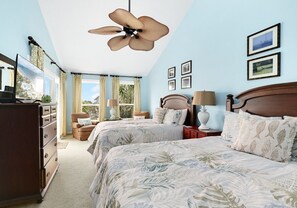 Ein Schlafzimmer mit zwei Betten, einem Deckenventilator, einem Schminktisch und einem Fenster mit Vorhängen.