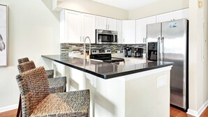 A modern kitchen with white cabinets, stainless steel appliances, and a central island with seating. - Seabrook Exclusives | 2942 Atrium (Seabrook Island)