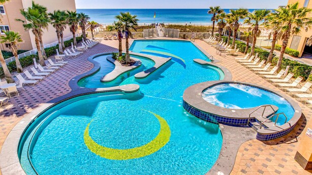 Uma piscina com design em forma de crescente lunar, rodeada por cadeiras de praia e palmeiras, com vista para o oceano.
