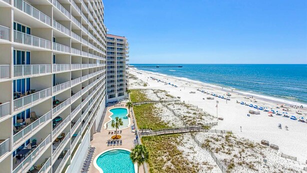 Ein Hochhaus-Hotel mit mehreren Balkonen, einem Schwimmbad und einem Strand mit Sonnenschirmen.