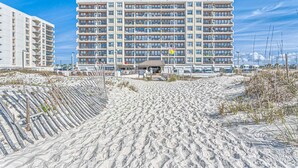 A multi-story hotel with a central entrance, a sandy beach in the foreground, and a clear blue sky. - 5th-Floor Beach View Condo w/Balcony, Shared Pool, Outdoor Shower, A/C, WiFi (Gulf Shores)
