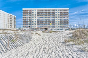 A multi-story hotel with a central entrance, a sandy beach in the foreground, and a clear blue sky. - 5th-Floor Beach View Condo w/Balcony, Shared Pool, Outdoor Shower, A/C, WiFi (Gulf Shores)
