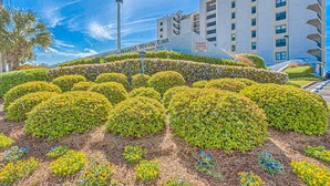 A landscaped area with neatly trimmed bushes and a building labeled 'Island Winds East' in the background. - 5th-Floor Beach View Condo w/Balcony, Shared Pool, Outdoor Shower, A/C, WiFi (Gulf Shores)