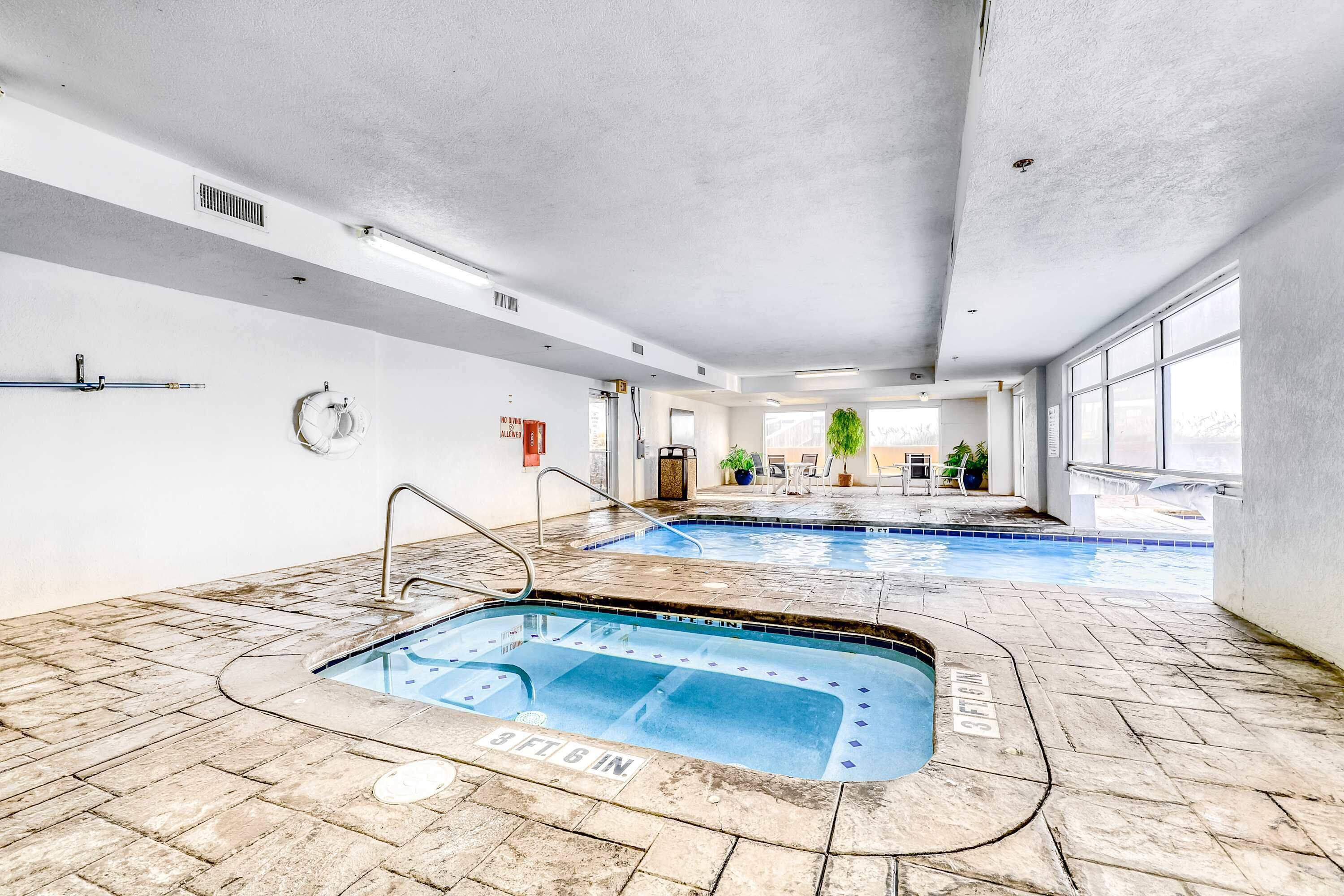Piscina interior com duas pistas de natação, chão em mosaico e vista para o exterior.