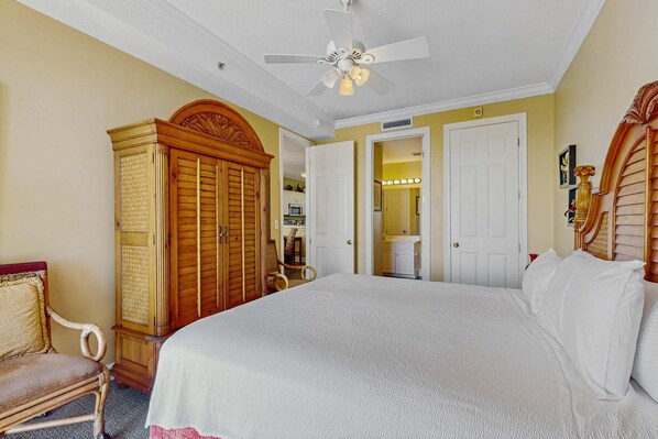 A bedroom with a large bed, a wooden wardrobe, a chair, and a ceiling fan. - Family-friendly Gulf-front condo with private balcony, hot tub, pool, & gym (Gulf Shores)