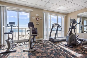 A gym with exercise equipment, large windows, and a carpeted floor. - Family-friendly Gulf-front condo with private balcony, hot tub, pool, & gym (Gulf Shores)