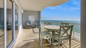 Een balkon met een tafel en stoelen, uitzicht op de oceaan, en een deur naar een andere kamer.