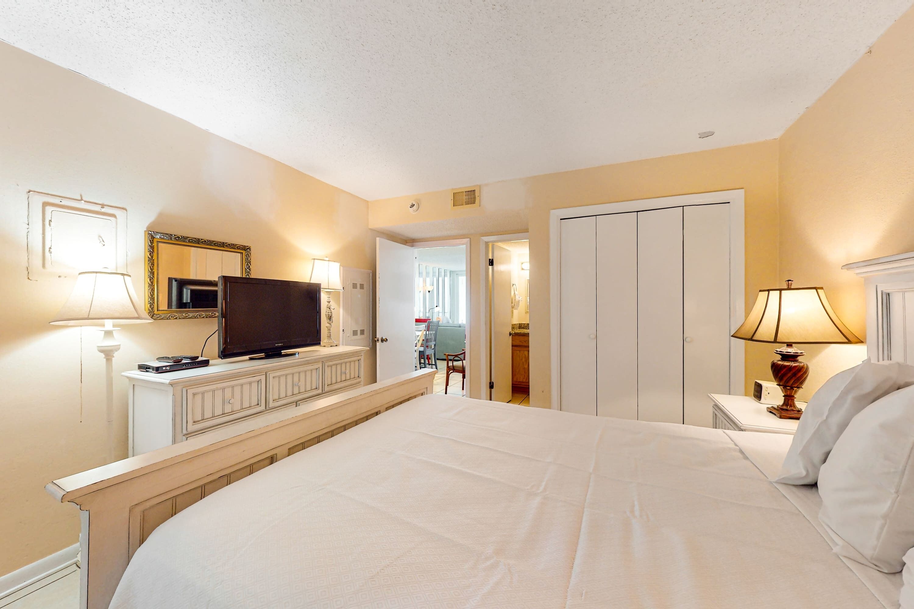 A hotel room with a bed, television, bedside table, lamp, and a wardrobe.
