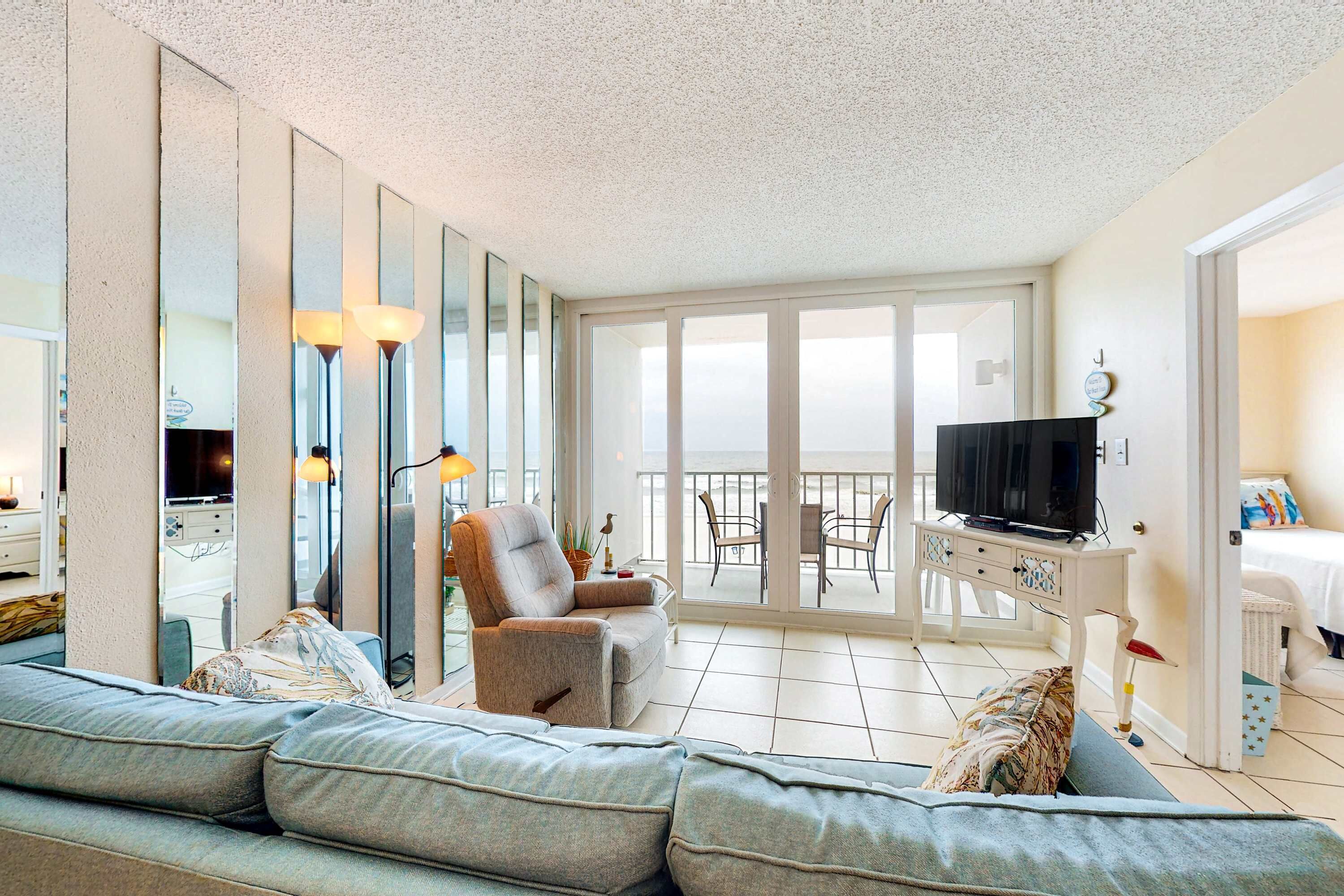 A modern living room with a sofa, armchair, TV, and balcony with chairs.