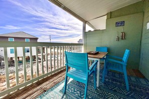 Eine überdachte Veranda mit Tisch und zwei Stühlen, ein Schild mit der Aufschrift 'Welcome to PORCH' sowie im Hintergrund ein Gebäude und ein Strand.