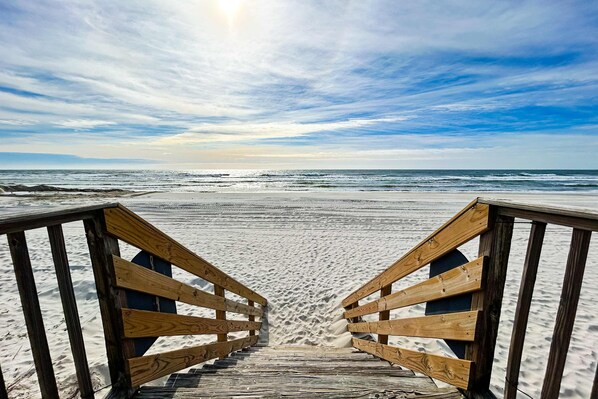 Ein hölzerner Steg führt zu einem Strand unter blauem Himmel.