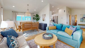 Una sala de estar con un sofá azul, una mesa de centro redonda de madera y un comedor con mesa y sillas de madera.