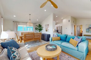 Una sala de estar con un sofá azul, una mesa de centro redonda de madera y un comedor con mesa y sillas de madera.