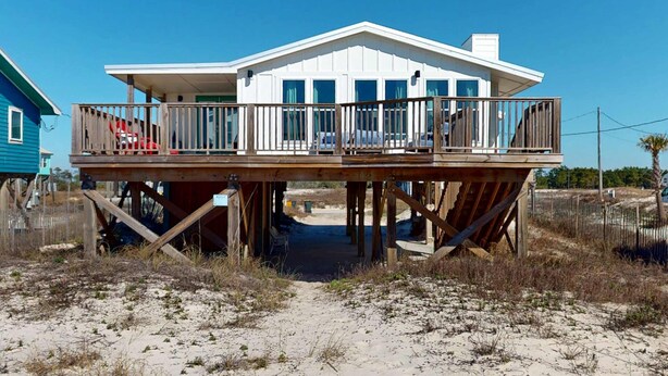 Una casa frente al mar con una terraza de madera, un porche cubierto y vista despejada al océano.