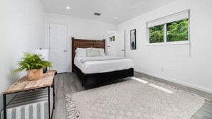 A bedroom with a bed, a small table with a plant, a window with a view of greenery, and a white door. - Your Downtown Getaway 2 (Fort Lauderdale)