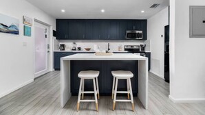 A modern kitchen with dark cabinets, a white island with stools, a microwave, and a coffee station. - Your Downtown Getaway 2 (Fort Lauderdale)