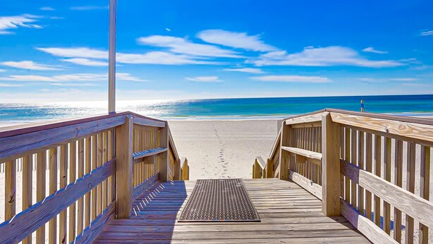 Una passerella di legno che conduce a una spiaggia sotto un cielo sereno.