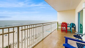 Un balcone con vista sulla spiaggia e sull'oceano, una ringhiera e sedie colorate.