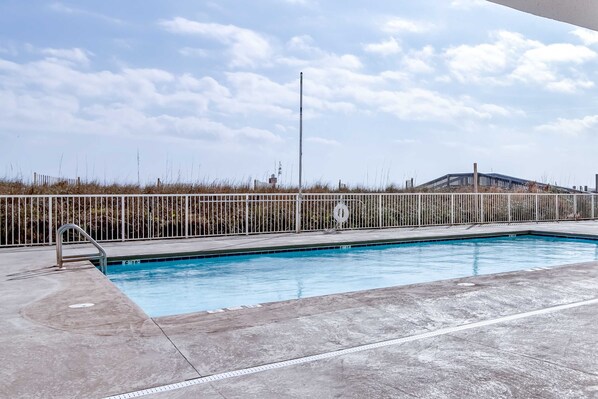 En swimmingpool med ett metallräcke, en betongplattform och en klar himmel.