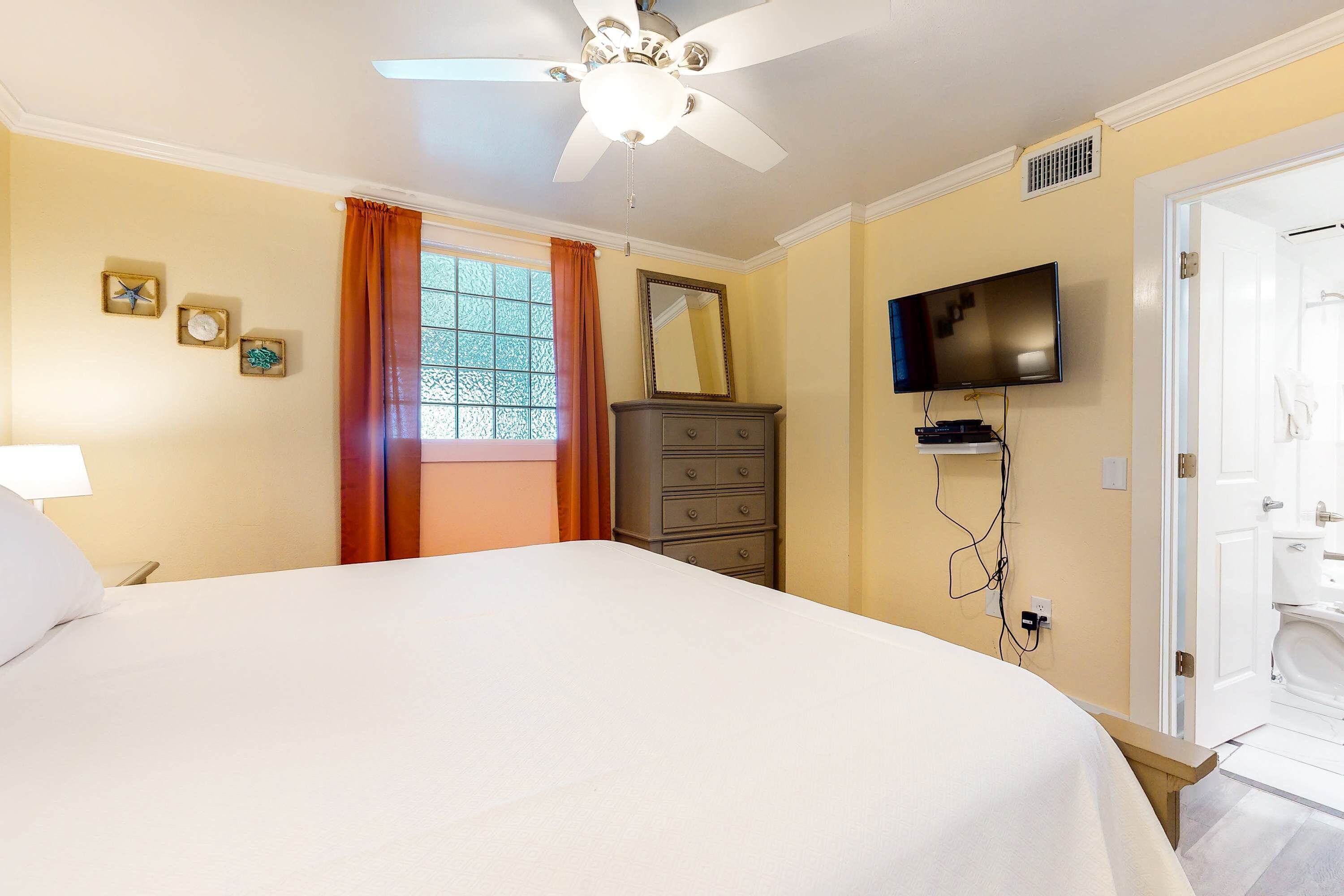 A hotel room with a bed, a dresser, a television, and a bathroom visible through an open door.