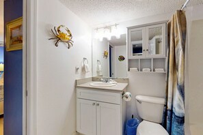 Casa de banho com lavatório, espelho, sanita e um caranguejo decorativo.