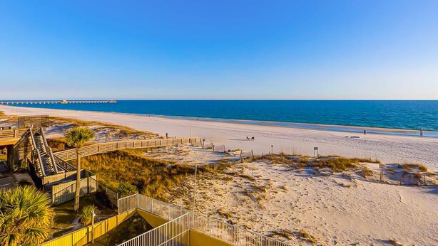 A beach with a wooden boardwalk, sandy dunes, and a clear blue sky. - Gulf-front 3rd-floor condo with outdoor pool, central AC, & balcony (Gulf Shores)