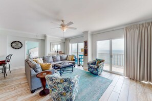 Ein geräumiges Wohnzimmer mit Deckenventilator, einer Couch, einem Couchtisch und Meerblick durch große Fenster.