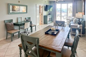 A spacious room with a wooden dining table, chairs, a sofa, a TV, and a balcony with a view. - Waterfront condo w balcony, boat slip, shared hot tubs, pools (Gulf Shores)