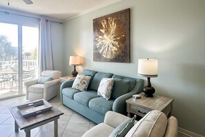 A living room with a teal sofa, two side tables with lamps, a coffee table, and a large abstract artwork on the wall. - Waterfront condo w balcony, boat slip, shared hot tubs, pools (Gulf Shores)