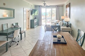 A spacious living area with a wooden dining table, a sofa, a TV mounted on the wall, and a balcony with a view. - Waterfront condo w balcony, boat slip, shared hot tubs, pools (Gulf Shores)