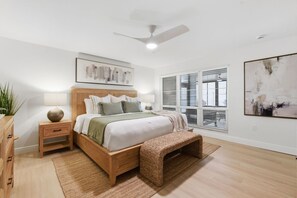 Ein modernes Schlafzimmer mit einem hölzernen Bett, Nachttischen, einem Deckenventilator und großen Fenstern.