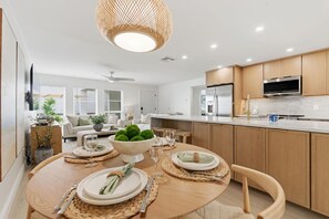 Eine moderne Küche mit Holzausstattung, einem Edelstahlkühlschrank und einem Essbereich mit rundem Tisch, Tellern und einer Schüssel grüner Äpfel.
