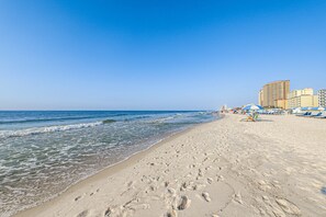 Ein Strand mit Fußspuren, einem klaren Himmel und Gebäuden im Hintergrund.