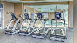 Four treadmills in a gym with a pool visible through the glass doors. - Gulf-Front Condo w Shaded Balcony, WiFi, AC & Shared Pools, Hot Tubs & Sauna (Gulf Shores)