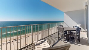 Un balcon avec vue sur la plage et l’océan, une table avec des chaises et un transat.