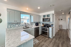 A modern kitchen with granite countertops, stainless steel appliances, and light blue cabinetry. - Waterview getaway with Private Pier, Balcony and Kayaks (Gulf Shores)