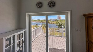 Uitzicht vanuit een kamer met een witte deur die leidt naar een terras met een balustrade, met zicht op een waterpartij en gebouwen.