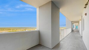 Un couloir aux murs blancs, un sol en béton et un balcon donnant sur la plage.