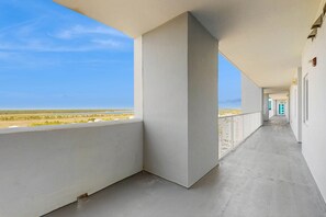 A corridor with white walls, a concrete floor, and a balcony with a view of the beach. - Bright beachfront condo w private balcony, zero-entry pool, gym, & hot tub (Gulf Shores)
