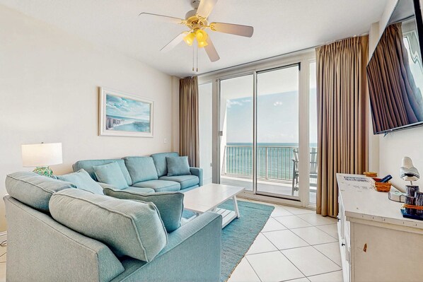 Une chambre d’hôtel avec un canapé, une table basse, une télévision et un balcon avec des rideaux.