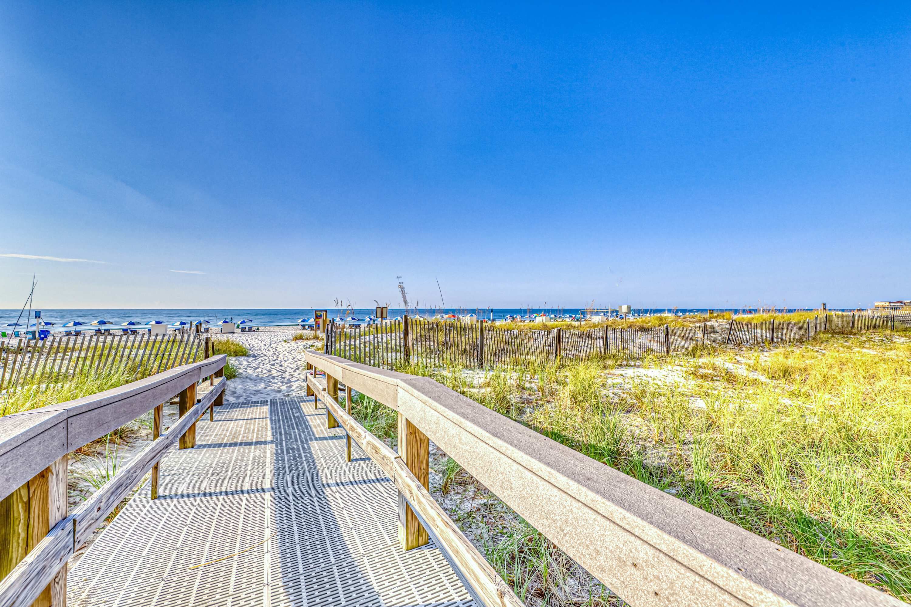 Ein hölzerner Steg führt zu einem Strand unter blauem Himmel.