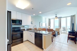 A kitchen with a refrigerator, oven, microwave, and dishwasher. There is a dining area with chairs and a table. - Beachfront Condo w Great Gulf View, Balcony & Shared Pools, Hot Tubs, Sauna & Gym (Gulf Shores)